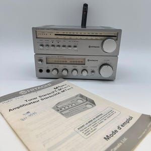 Puede incluir: Un sintonizador estéreo Hitachi modelo FT-M1MKII plateado apilado sobre un amplificador estéreo Hitachi modelo HA-M1MKII a juego. Un manual de papel titulado Tuner Stereo (FT-M1MKII) y Amplificateur Stereo (HA-M1MKII) con la marca Hitachi está al frente.