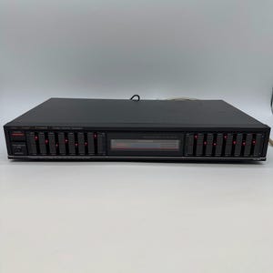 May include: A black Fisher stereo graphic equalizer featuring two banks of vertical sliders with red LED indicators. The front panel includes a power button, a tape monitor switch, and a central display area. The model number EQ-867 is printed on the right.