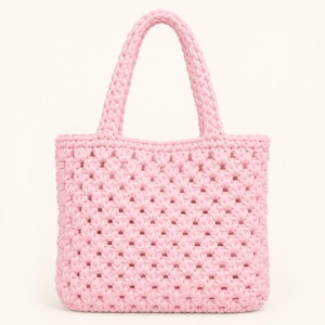 Puede incluir: Un bolso tote de color rosa claro elaborado con un patrón de crochet de cuadrados de la abuela texturizados. El bolso cuenta con dos asas integradas y un cuerpo rectangular con un diseño calado, mostrando un hilo rosa pastel uniforme.
