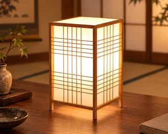 May include: A rectangular table lamp featuring a light-colored wooden frame with a grid pattern and translucent white panels. The lamp emits a warm, soft glow from within, illuminating the surrounding area with a gentle light through the paper-like sides.