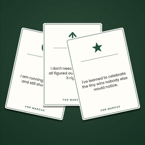 May include: Three white rectangular cards with rounded corners, featuring dark green text and symbols. Each card displays a unique phrase, a horizontal line, a symbol, and the text FOR MARCUS at the bottom. The cards are arranged in a fan shape.