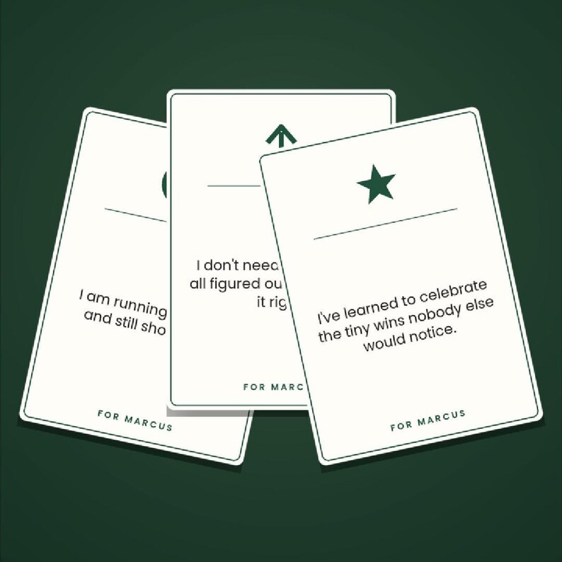 May include: Three white rectangular cards with rounded corners, featuring dark green text and symbols. Each card displays a unique phrase, a horizontal line, a symbol, and the text FOR MARCUS at the bottom. The cards are arranged in a fan shape.