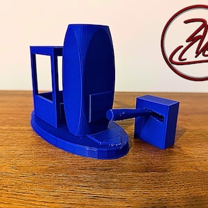 May include: A 3D-printed blue desk organizer featuring a central oval pillar, a rectangular frame section, and a separate small block with a protruding horizontal arm. The object displays a smooth matte finish and includes a circular logo with the text 3Desk.