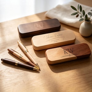 May include: Three rectangular wooden pen cases and three matching pens with gold-tone accents. One dark wood case features the initials LS, a light wood case is engraved with Shani Rogers Astrochemist EST 2025, and a two-tone case features the initials KW.