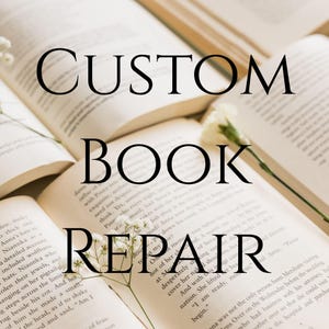 Op de afbeelding: Open pagina's van een vintage boek met zichtbare gedrukte tekst, vergezeld van kleine witte bloemen. De tekst CUSTOM BOOK REPAIR is in een groot zwart schreeflettertype over het midden van de open boekpagina's en bloemen geplaatst.