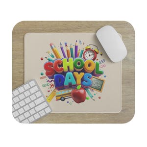 Może przedstawiać: Prostokątna podkładka pod mysz o jasnobeżowej powierzchni z kolorową grafiką przedstawiającą napis SCHOOL DAYS w formie liter 3D. Wzór zawiera czerwone jabłko, żółty autobus szkolny, ołówki, czerwony budzik oraz małą tablicę szkolną.