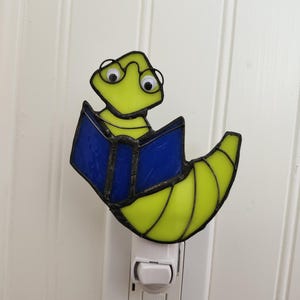 May include: A stained glass night light shaped like a worm wearing glasses and reading a blue book. The night light plugs into a standard electrical outlet.
