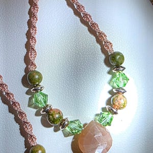 May include: A pair of dangle earrings featuring a rose gold twisted wire frame. Each earring is adorned with round green mottled beads, faceted lime green crystal beads, silver-toned spacers, and a single faceted peach-colored teardrop stone.