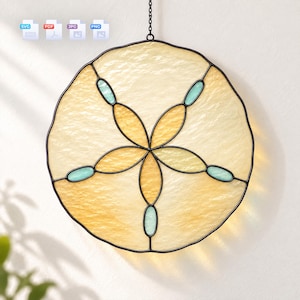May include: A circular stained glass suncatcher featuring a sand dollar design with textured pale yellow glass panels, accented by five small oval light blue glass pieces, all encased in a dark metal frame and suspended by a thin black chain.