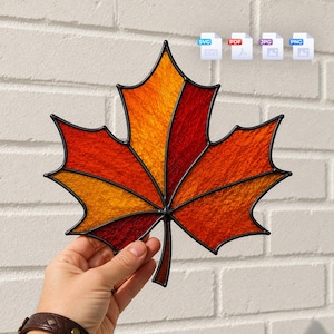 Puede incluir: Un atrapasoles de vidrieras con forma de hoja de arce, con paneles texturizados en tonos naranja, amarillo y rojo intenso, delineados con líneas de soldadura de metal negro. Incluye iconos de archivos digitales SVG, PDF, JPG y PNG en la parte superior.