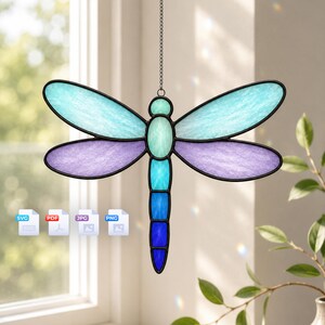 May include: A dragonfly suncatcher featuring stained glass wings in shades of light blue and purple, with a body composed of segments in light blue, cyan, and dark blue. The piece is framed in black metal and hangs from a thin metal chain.
