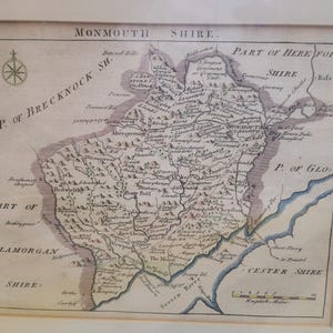 May include: An antique-style map of Monmouth Shire featuring detailed topography, town names, and a compass rose. The map includes text labels for surrounding regions like Brecknock Shire, Hereford Shire, and Glamorgan Shire, with a scale in English miles.