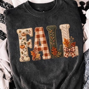 May include: A charcoal gray crewneck sweatshirt featuring the word FALL in large block letters. Each letter has a unique texture: the F has pumpkins, the A has a brown plaid pattern, the L has green corduroy with leaves, and the L has a cable knit.