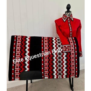 May include: A red long-sleeve shirt with a black, white, and red patterned collar and cuffs, paired with a matching rectangular saddle pad featuring a black, red, and white geometric zigzag and square pattern with the text Elite Equestrian Hub.
