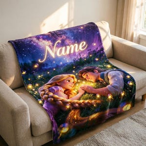 Könnte beinhalten: Eine weiche Wohndecke mit einem aufgedruckten Motiv zweier animierter Figuren mit langem blonden und braunen Haar, die nachts auf einer Wiese sitzen, umgeben von leuchtenden Lichtern unter einem violetten Sternenhimmel mit dem Wort Name.