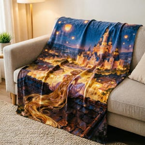 May include: A soft throw blanket featuring a printed scene of a character with long blonde hair sitting on a rooftop overlooking a glowing castle at night. The sky is filled with floating lanterns, and the town below is illuminated with warm yellow lights.