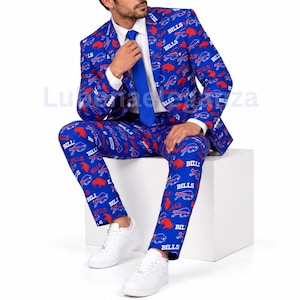 Puede incluir: Un traje azul de chaqueta y pantalón con un estampado repetitivo del logotipo rojo de los Buffalo Bills y la palabra Bills en blanco. El conjunto incluye una camisa blanca de botones y una corbata azul lisa que combina con el diseño.