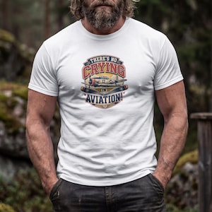 May include: A white short-sleeved t-shirt featuring a central graphic print of a vintage propeller airplane. The design includes the text "THERE'S NO CRYING IN AVIATION!" in bold red and blue lettering, surrounded by a circular emblem with stars.
