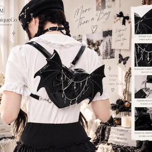 Puede incluir: Una mochila negra con forma de corazón hecha de material brillante, con alas de murciélago en los laterales y detalles de cadenas plateadas con pequeños dijes de cruz. Incluye correas ajustables, herrajes metálicos y un cierre de cremallera.