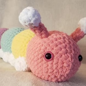 May include: A crocheted caterpillar plush toy with a pink body, yellow, green, and purple stripes, and white fluffy antennae.