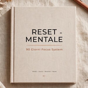 Può includere: Un libro con copertina rigida color beige con il testo RESET - MENTALE, 90 Giorni Focus System, e ADHD • Focus • Routine • Reset stampato sulla copertina. Il libro ha una finitura testurizzata simile al tessuto ed è posizionato in piano.