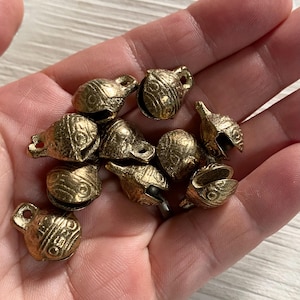 May include: A collection of small, gold-coloured metal bells with intricate designs. The bells have a rounded shape and a small opening at the top for hanging.