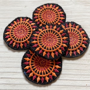 Könnte beinhalten: Fünf runde gestickte Aufnäher mit schwarzem Hintergrund und einem roten und orangefarbenen Mandala-Design.