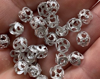 May include: A collection of silver metal bead caps with a decorative openwork design. The caps are small and round, with a delicate pattern of holes and curves.