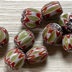 Pode incluir: Uma coleção de oito contas de vidro verde, branco e vermelho com um padrão listrado. As contas são de forma oval e têm um acabamento brilhante.