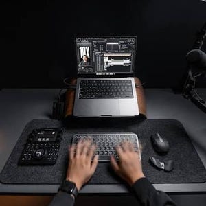 Könnte beinhalten: Ein silberner Laptop auf einem Holzständer, der Videobearbeitungssoftware mit dem Text 10X anzeigt, eine schwarze Tastatur, eine schwarze Maus und ein schwarzer Konsolen-Controller auf einer dunkelgrauen Schreibtischunterlage.