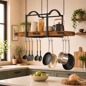 May include: A rectangular hanging pot rack featuring a dark metal frame suspended by chains, with a wooden shelf holding a glass jar, a white pitcher, and a dark kettle. Below, metal hooks hold various kitchen utensils and metal pans.