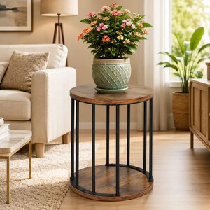 May include: A round side table with a dark wood grain top and bottom shelf, supported by vertical black metal bars. A light green ceramic pot with a textured lattice pattern sits on the table, containing a flowering plant with pink and orange blooms.