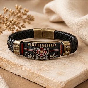 May include: A black braided leather bracelet featuring a central antique brass plate with the text FIREFIGHTER, a red and gold emblem, and the words HONOR, COURAGE, SACRIFICE. The side plates are engraved with STRENGTH & HONOR and VALOR & PRIDE.