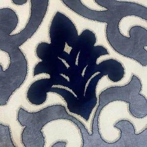 May include: A fabric featuring a repeating damask pattern in deep navy blue and light cream. The navy blue sections have a soft, velvet-like texture, while the cream areas are outlined with a thin, shimmering gold metallic thread border.