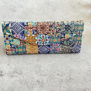 May include: A rectangular eyeglass case featuring a vibrant, multi-colored mosaic tile pattern. The design consists of various geometric and floral motifs in shades of blue, yellow, green, red, and white, arranged in a repeating grid across the surface.