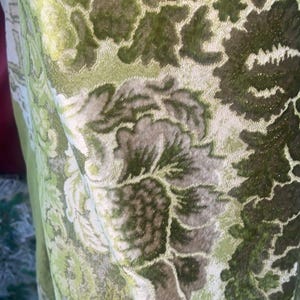 May include: A fabric textile featuring a dense, raised floral damask pattern in shades of sage green, olive green, and muted grey. The material has a textured, velvet-like appearance with intricate botanical motifs woven throughout the surface.