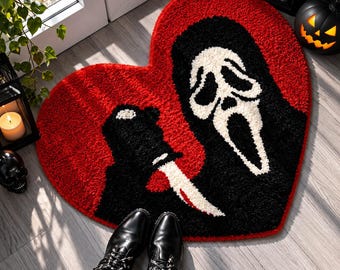 Pode incluir: Um tapete tufado em forma de coração com um fundo vermelho vibrante e um gráfico a preto e branco de uma figura mascarada a segurar uma faca. O design inclui a icónica máscara branca alongada e uma lâmina afiada e texturizada.