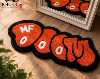 Pode incluir: Um tapete tufado com um design vibrante em laranja e preto com letras brancas que soletram MF DOOM. O tapete tem uma forma arredondada e orgânica com uma borda preta espessa e uma superfície texturizada, refletida num espelho colocado atrás.
