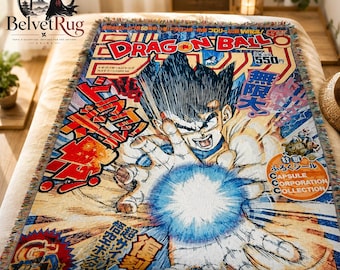 Pode incluir: Uma manta tecida com a estampa de uma capa de mangá Dragon Ball. O design mostra um personagem de cabelo espetado lançando uma rajada de energia azul brilhante, cercado por texto em japonês, o logotipo Dragon Ball e o logotipo Capsule Corporation.