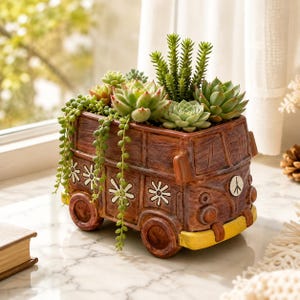 May include: A brown ceramic planter shaped like a vintage van with white flower decals and a peace sign emblem on the front. The van features a yellow front bumper and is filled with various green succulents, including a trailing string of pearls.
