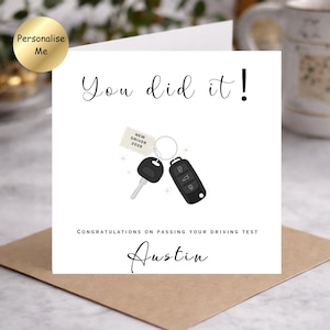 May include: A square greeting card with a white background featuring the text You did it! at the top. In the centre is an illustration of a key ring with a car key, a remote fob, and a tag reading NEW DRIVER 2026. Below is the text CONGRATULATIONS ON PASSING YOUR DRIVING TEST and the name Austin.