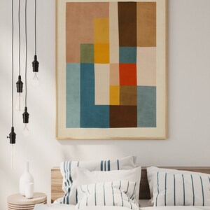 Może przedstawiać: Abstrakcyjny wydruk artystyczny w drewnianej ramie. Grafika przedstawia geometryczny wz&oacute;r z blokami kolor&oacute;w w odcieniach niebieskiego, brązowego, ż&oacute;łtego i czerwonego. Nad ł&oacute;żkiem z pasiastymi poduszkami i drewnianym zagł&oacute;wkiem wisi wydruk.