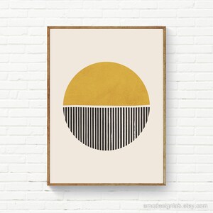 May include: Abstract art print in a wooden frame. The artwork features a gold half-circle above a black and white striped half-circle on a cream background. The print is mounted on a white brick wall.