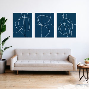 May include: Three abstract art prints with white lines on a dark blue background. The prints are arranged in a row on a white wall above a light gray couch.