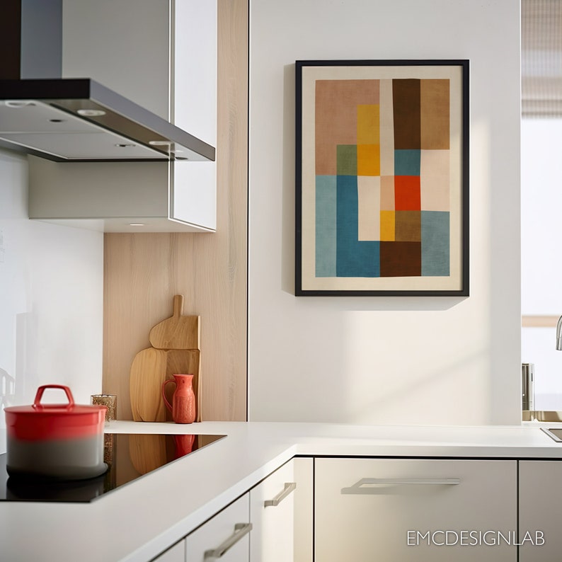 Może przedstawiać: Oprawiony abstrakcyjny wydruk artystyczny z czarną obw&oacute;dką wisi na białej ścianie w nowoczesnej kuchni. Grafika przedstawia geometryczny wz&oacute;r z blokami kolor&oacute;w, w tym brązowym, niebieskim, ż&oacute;łtym i czerwonym. Kuchnia ma białe szafki i czerwony garnek.