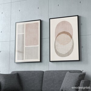 Pode incluir: Duas impress&otilde;es de arte abstrata emolduradas com formas geom&eacute;tricas em tons de marrom, rosa e branco. As impress&otilde;es est&atilde;o penduradas em uma parede de concreto acima de um sof&aacute; cinza.