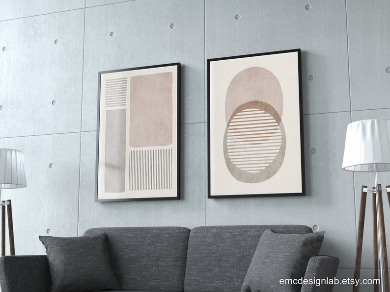 Pode incluir: Duas impress&otilde;es de arte abstrata emolduradas com formas geom&eacute;tricas em tons de marrom, rosa e branco. As impress&otilde;es est&atilde;o penduradas em uma parede de concreto acima de um sof&aacute; cinza.