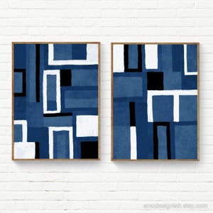 May include: Two abstract geometric paintings in a blue, white, and black color scheme. The paintings are framed in a light wood frame and are hanging on a white brick wall.