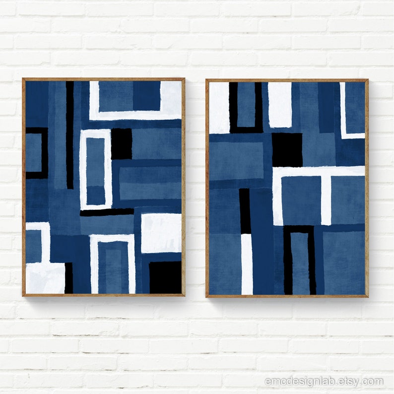 May include: Two abstract geometric paintings in a blue, white, and black color scheme. The paintings are framed in a light wood frame and are hanging on a white brick wall.