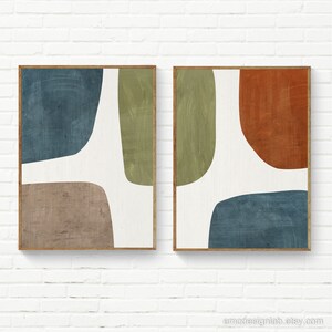 May include: Two abstract art prints with a white background and colorful shapes. The shapes are in shades of blue, green, brown, and orange. The prints are framed in a natural wood frame.